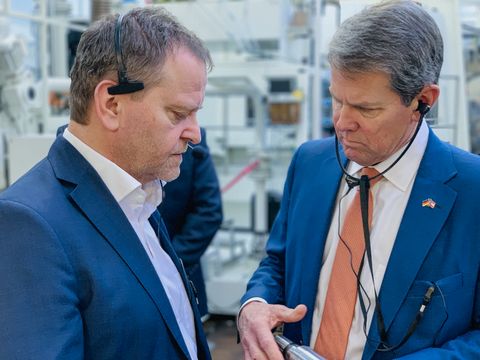 Geschäftsführung Jürgen Häring mit dem Besuch des Gouverneu stehen mit Kopfhörer an einer Maschine